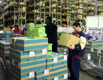 Several people packing and lifting boxes in a large warehouse.